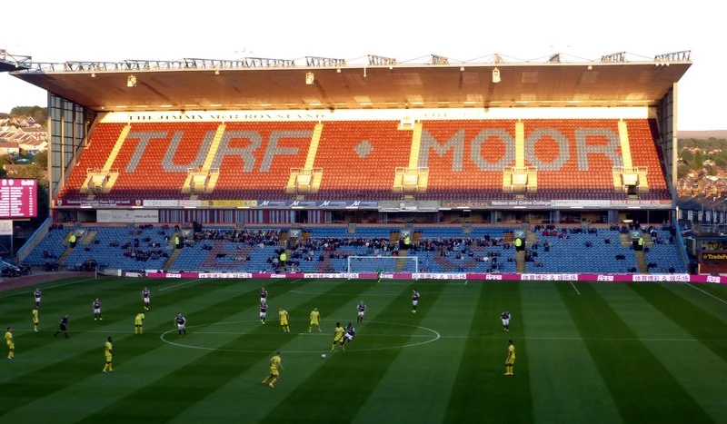 A real match under way at Turf Moor, seen across the pitch towards the stand spelling TURF MOOR.